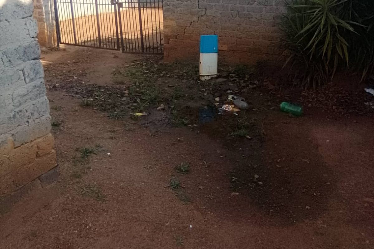 A rear outdoor area featuring a metal gate and a brick boundary wall with visible structural cracking and unpaved ground.