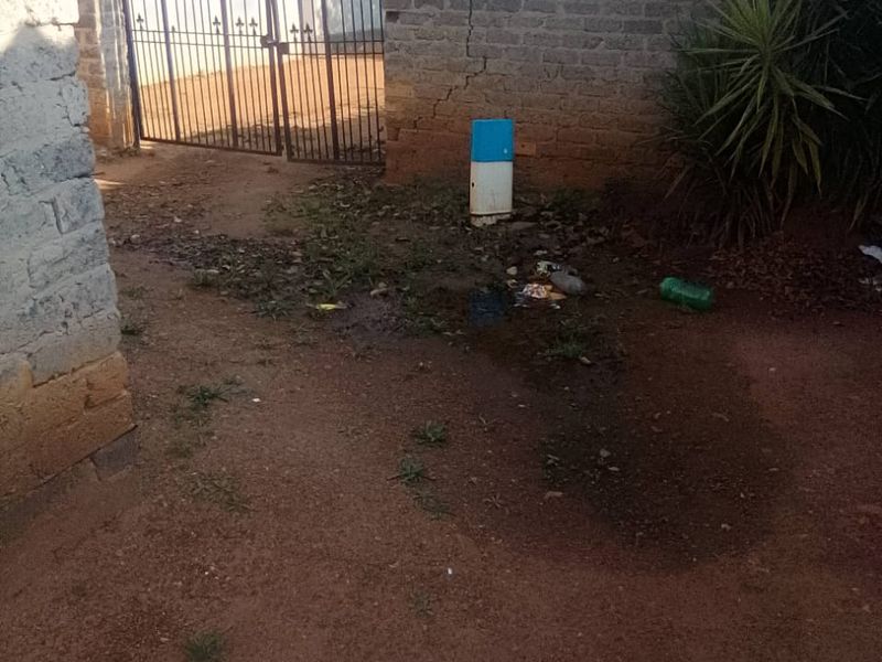A rear outdoor area featuring a metal gate and a brick boundary wall with visible structural cracking and unpaved ground.