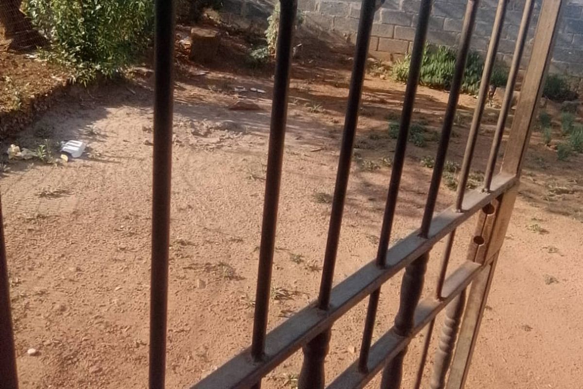 A view of a rear yard area featuring a metal security gate, concrete block boundary wall, and an unlandscaped sandy ground surface.