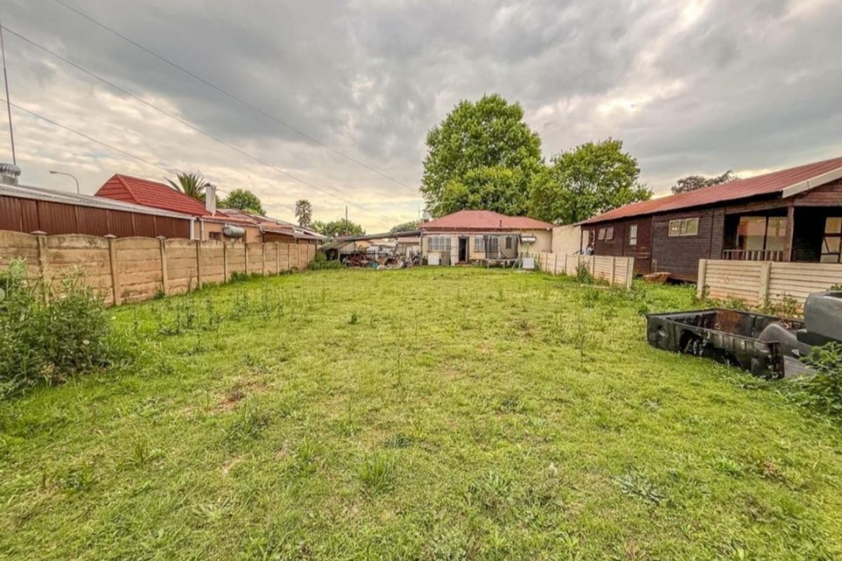 Spacious rear yard featuring a large lawn area enclosed by precast concrete boundary walls and adjacent residential structures.