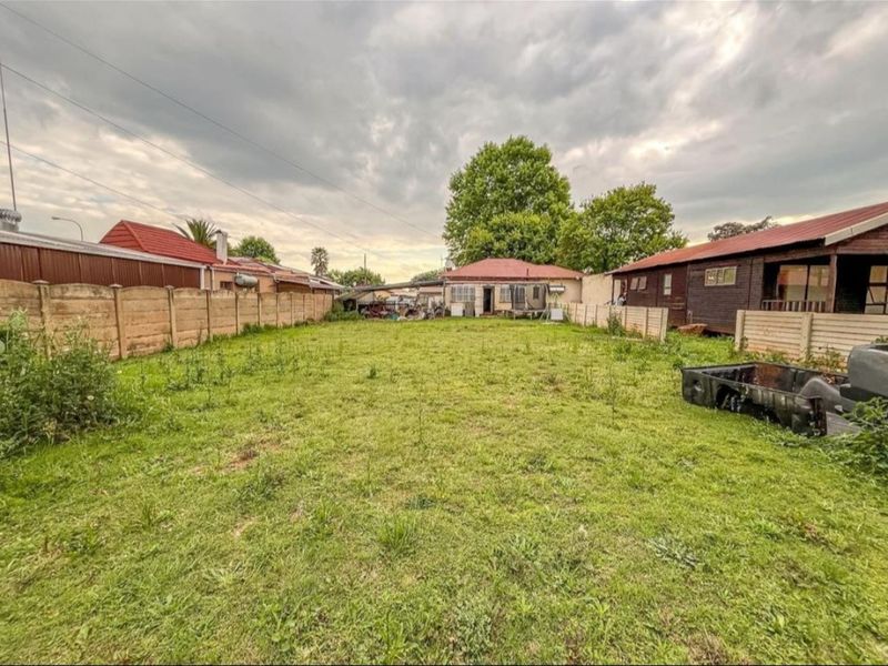 Spacious rear yard featuring a large lawn area enclosed by precast concrete boundary walls and adjacent residential structures.
