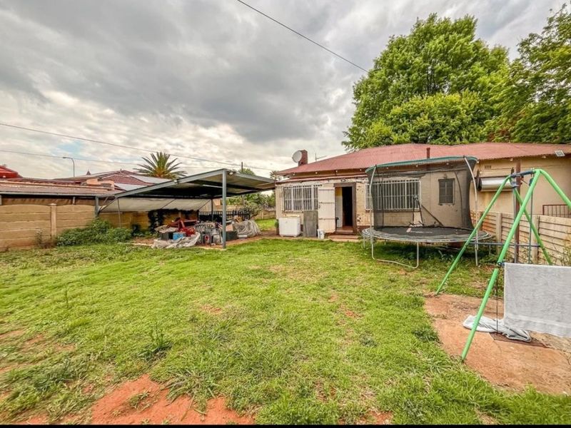 Rear view of the property featuring a lawn, a metal carport structure, and a brick building exterior with security bars on the windows.