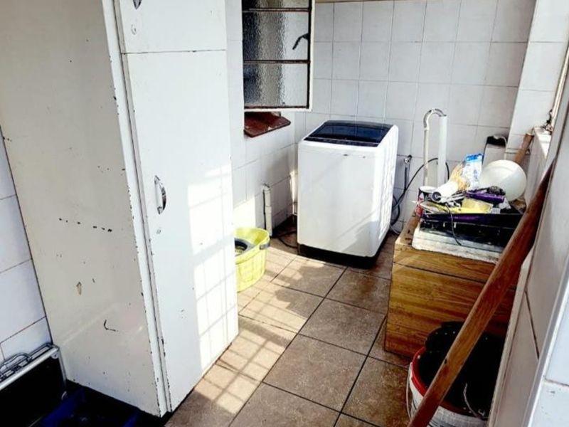 A functional laundry area featuring tiled flooring, wall tiling, and built-in storage cabinetry with dedicated plumbing connections.