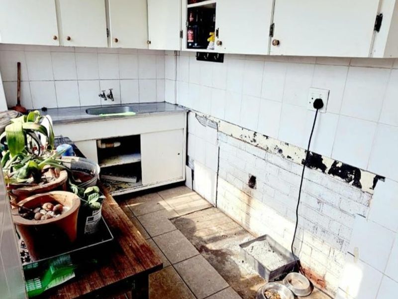 A dated kitchen requiring significant renovation, featuring original cabinetry, tiled splashbacks, and visible wall damage, offering potential for a complete modern transformation.