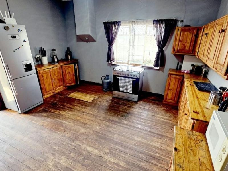 A rustic kitchen featuring wooden cabinetry, timber countertops, and a freestanding gas stove, offering a traditional aesthetic with potential for modern updates.