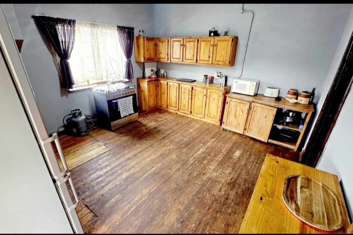 A rustic kitchen featuring wooden cabinetry, a gas stove, and original hardwood flooring, offering potential for modernization and cosmetic updates.