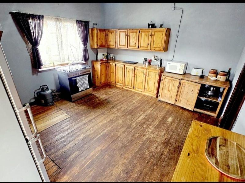A rustic kitchen featuring wooden cabinetry, a gas stove, and original hardwood flooring, offering potential for modernization and cosmetic updates.