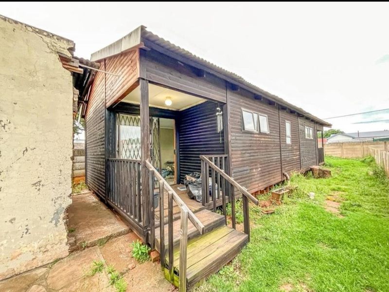 Rear view of a timber-clad structure featuring a small wooden deck, sliding door access, and corrugated metal roofing, set within a grassed yard area.