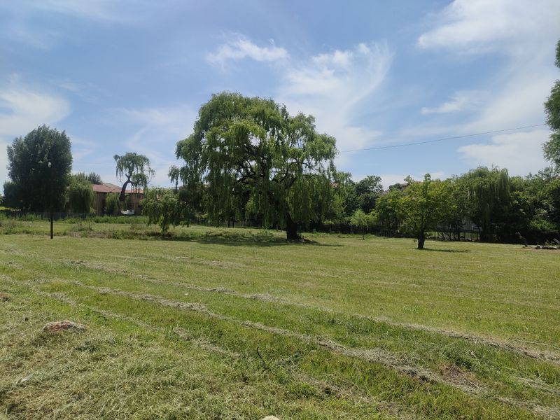 A spacious, level residential vacant land plot featuring established mature trees and a well-maintained grass lawn.
