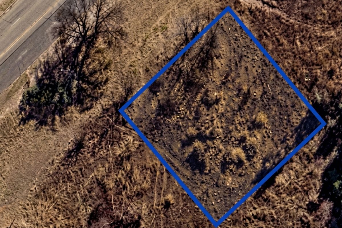 An aerial view of a vacant residential plot of land with road access, showing natural vegetation and clear boundary markings.