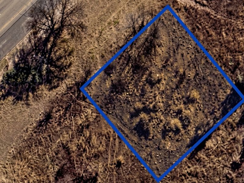 An aerial view of a vacant residential plot of land with road access, showing natural vegetation and clear boundary markings.
