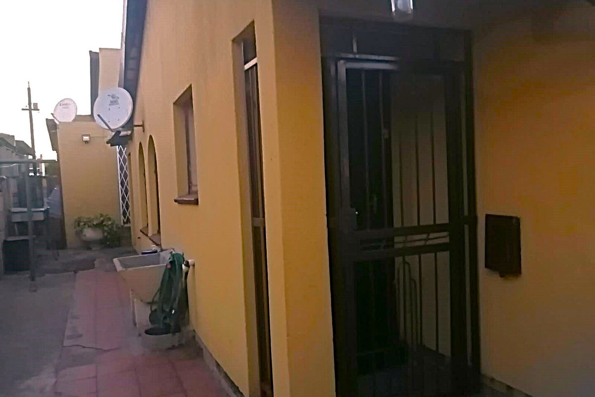 Rear exterior view of the property featuring a security gate, utility sink, and tiled patio area.