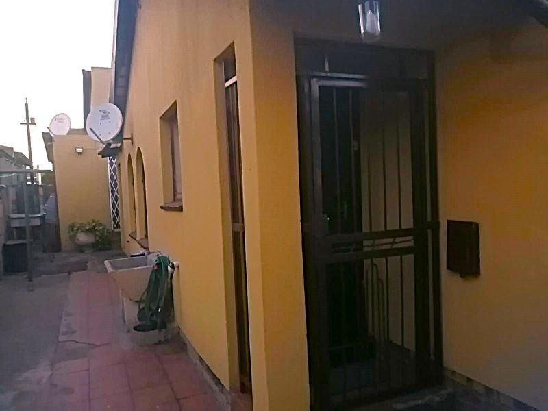 Rear exterior view of the property featuring a security gate, utility sink, and tiled patio area.