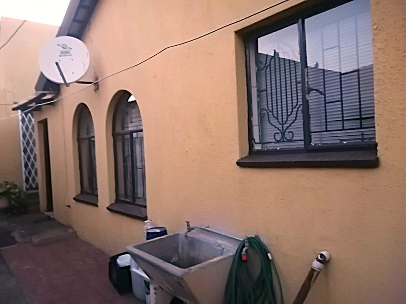 Rear exterior view of the property featuring arched windows with security bars, a utility sink, and a paved patio area.