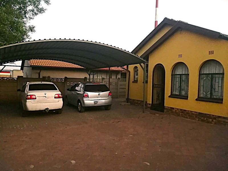 Front exterior view of the property featuring a covered carport, paved driveway, and arched window detailing on the main building facade.