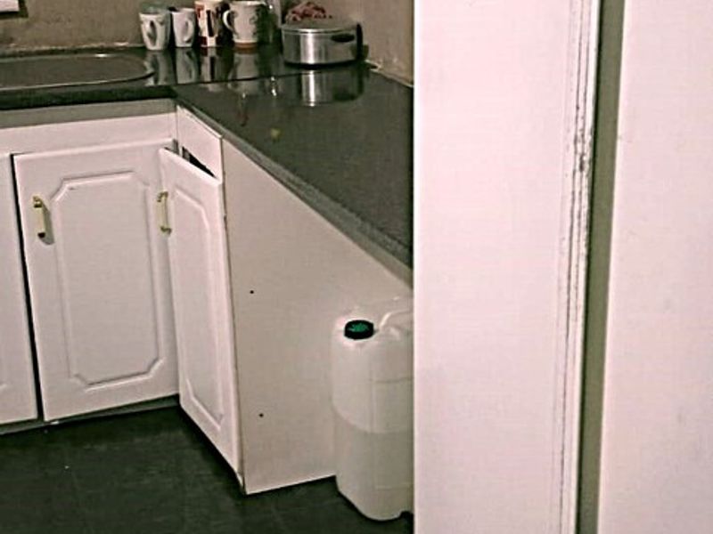 A small kitchen area featuring dark tiled flooring, stone countertops, and white cabinetry with visible damage to the lower cabinet door.