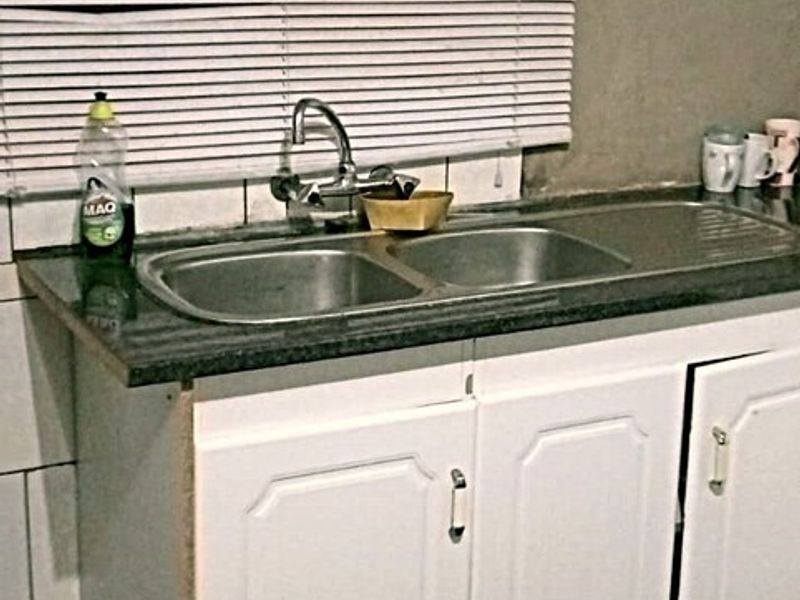 A compact kitchen area featuring a double bowl stainless steel sink, granite countertop, and white cabinetry, requiring minor cosmetic updates.