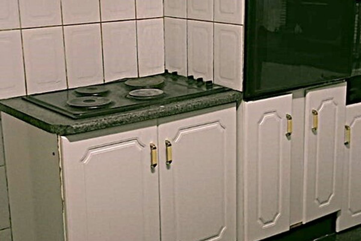 A dated kitchen featuring white cabinetry, a built-in oven, electric hob, and dark tiled flooring, offering potential for a modern renovation.