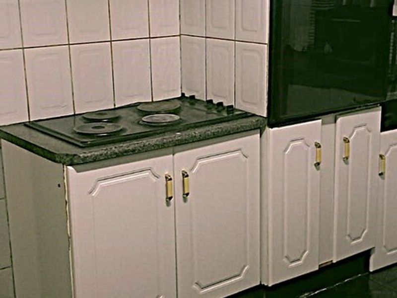A dated kitchen featuring white cabinetry, a built-in oven, electric hob, and dark tiled flooring, offering potential for a modern renovation.
