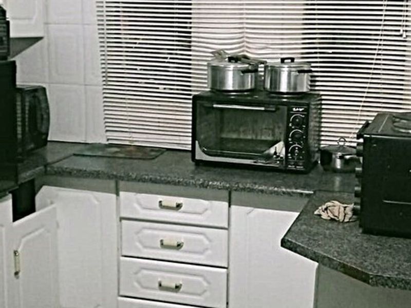 A compact kitchen featuring white cabinetry, dark laminate countertops, and a tiled backsplash, offering a functional layout with potential for modern updates.