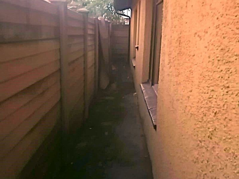 A narrow side passage featuring a timber boundary fence and concrete pathway along the exterior stucco wall of the house.