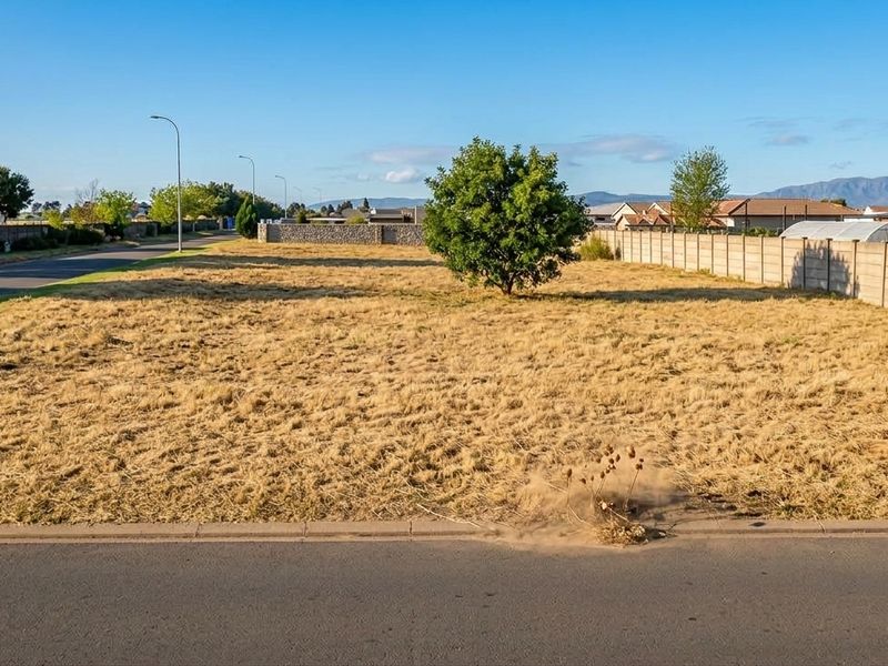A vacant residential plot featuring a level grass surface, concrete boundary walling, and direct street access in a established neighborhood.