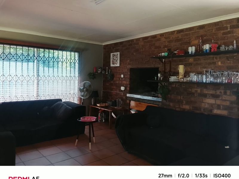 Living room featuring an exposed brick feature wall with a built-in fireplace, tiled flooring, and large windows secured with metal security gates.