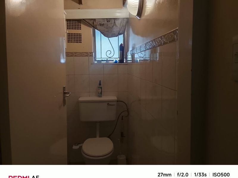 A compact bathroom featuring dated ceramic wall tiles, a standard toilet, and a small window with security bars.