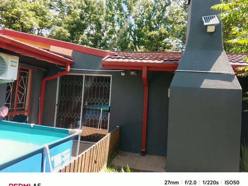 Outdoor pool area featuring a large external fireplace, sliding glass doors with security gates, and a tiled roof with integrated guttering.