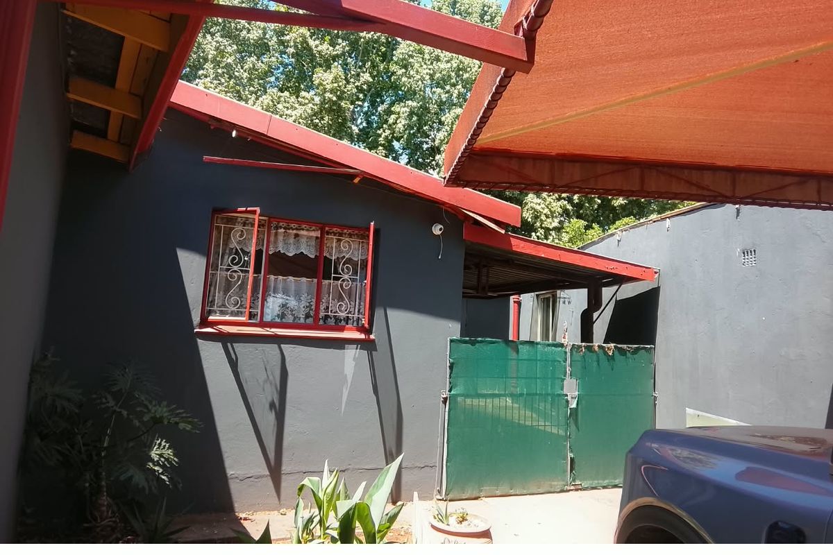 Rear exterior view of the property featuring a retractable awning, security gate, and security bars on the window.