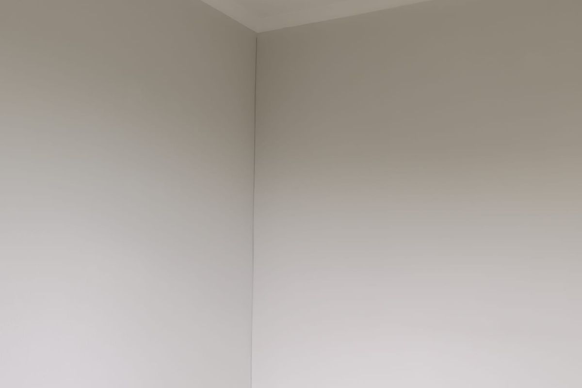 A corner view of an empty room featuring neutral painted walls, tiled flooring, and a standard electrical outlet.