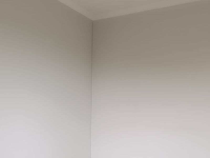 A corner view of an empty room featuring neutral painted walls, tiled flooring, and a standard electrical outlet.
