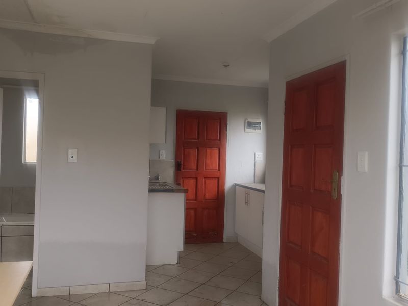 An open-plan living and kitchen area featuring tiled flooring, built-in cabinetry, and timber doors, requiring some cosmetic maintenance and updates.