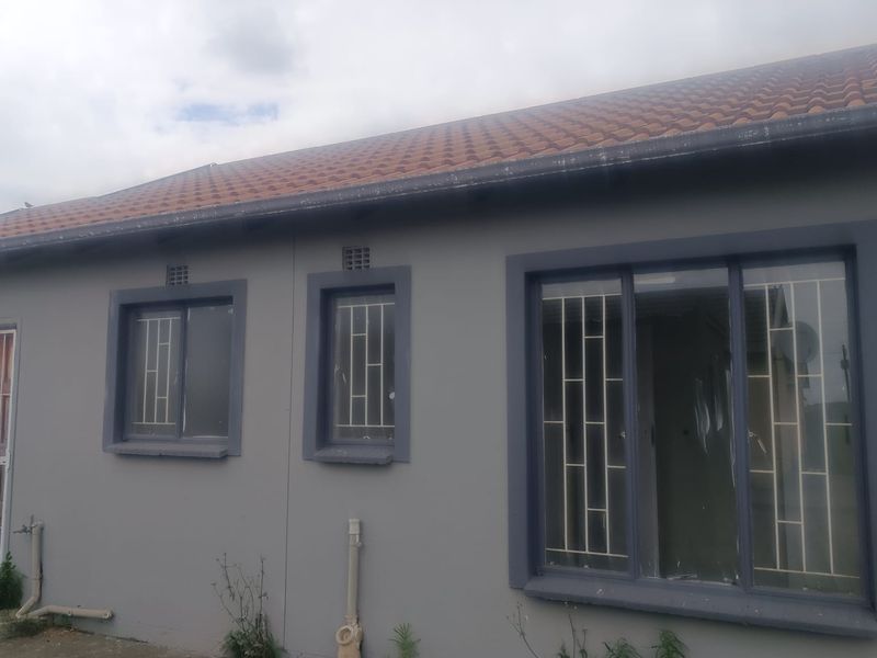 Rear exterior view of the house featuring terracotta roof tiles, security bars on windows, and external plumbing fixtures.