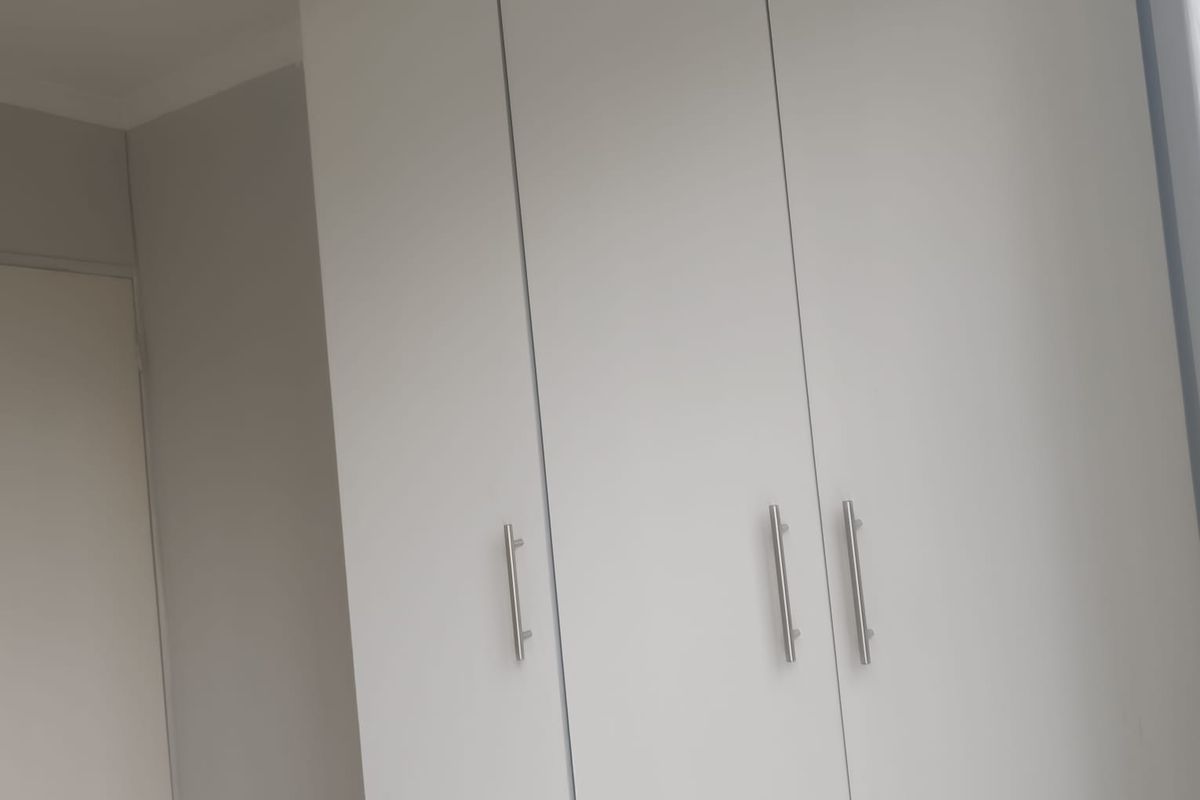 A clean bedroom interior featuring modern white built-in cupboards with sleek metal handles.