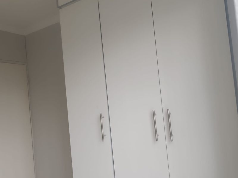 A clean bedroom interior featuring modern white built-in cupboards with sleek metal handles.