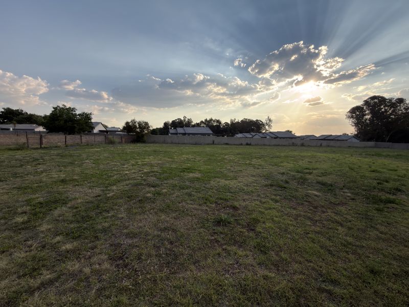 A spacious, level vacant residential plot enclosed by a perimeter wall, offering a clear area ready for development.