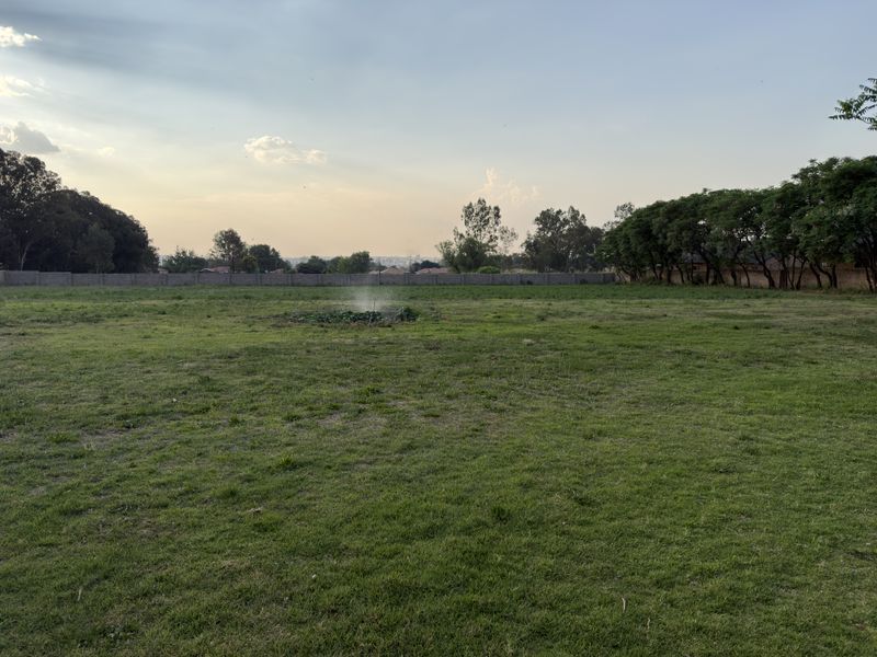 A spacious, level residential plot featuring a well-maintained lawn and a secure perimeter wall, offering potential for future development.