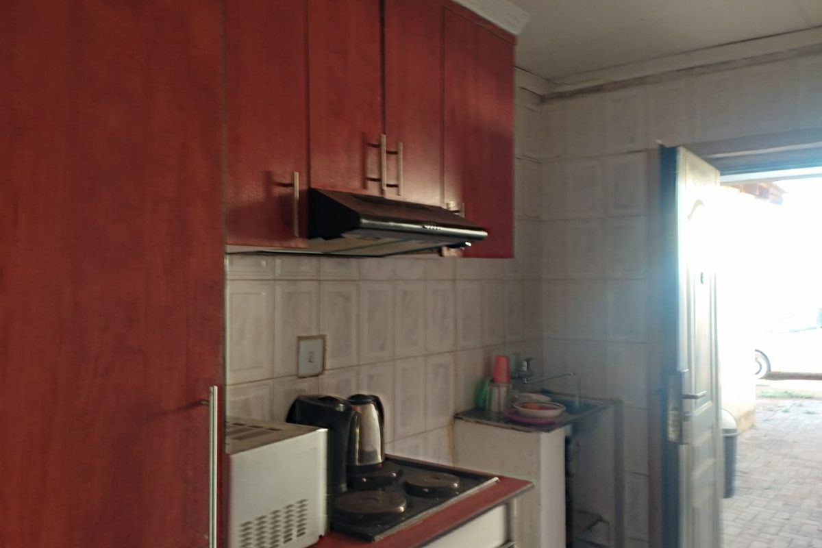 A compact kitchen featuring built-in cabinetry, a tiled backsplash, and a functional hob with an extractor fan, providing direct access to the exterior.