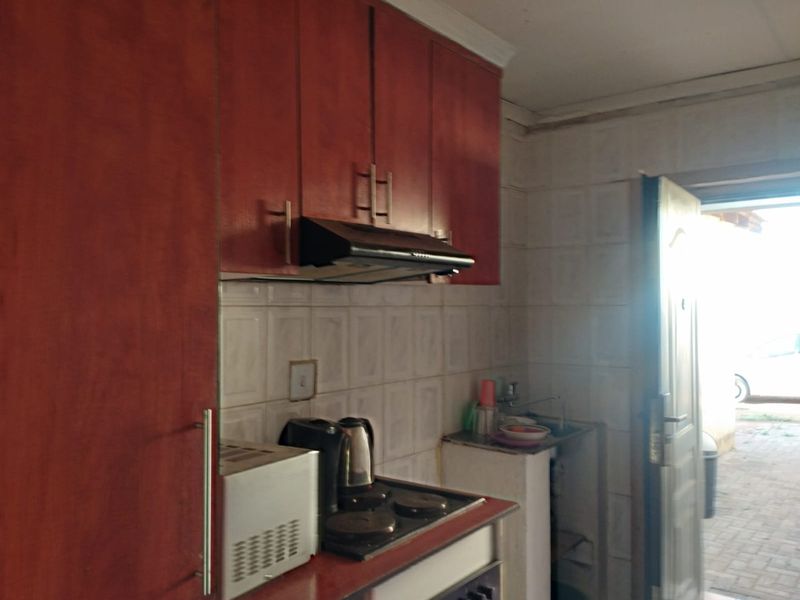 A compact kitchen featuring built-in cabinetry, a tiled backsplash, and a functional hob with an extractor fan, providing direct access to the exterior.