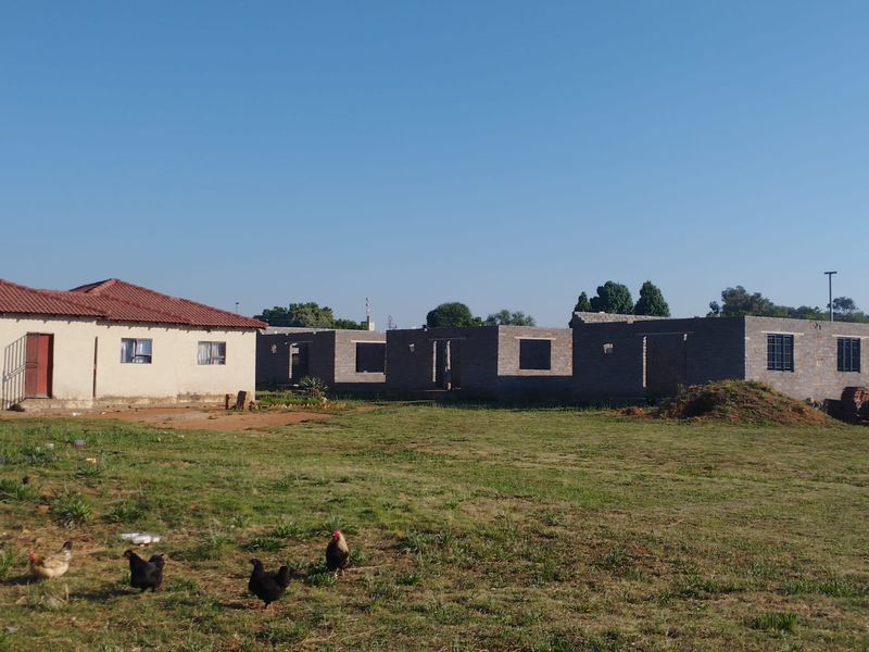 View of an existing dwelling alongside a partially constructed masonry building structure on a large plot of land.