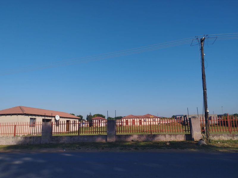 A street-level view of a residential property featuring a tiled roof house enclosed by a masonry boundary wall with integrated electric fencing.