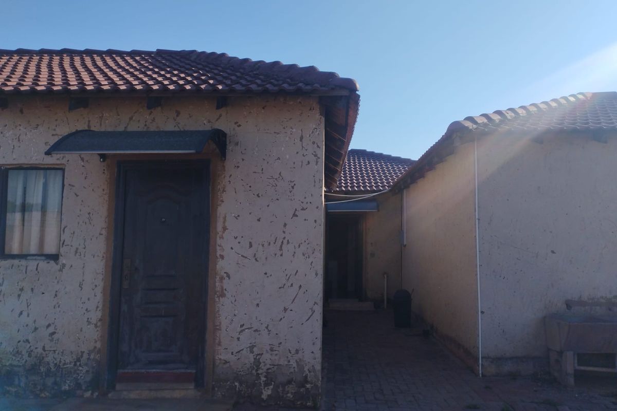 Rear exterior view of the property showing a paved walkway between building sections, featuring tiled roofing and weathered exterior wall finishes.