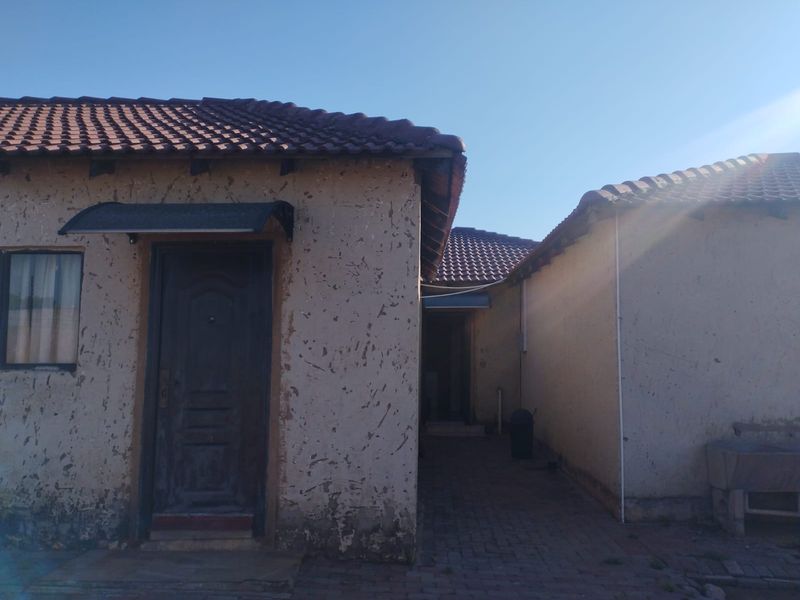 Rear exterior view of the property showing a paved walkway between building sections, featuring tiled roofing and weathered exterior wall finishes.