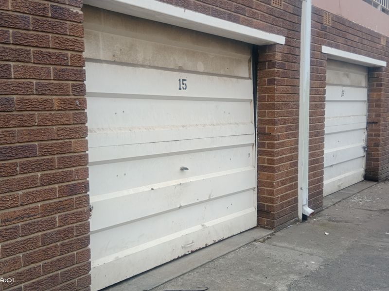 A row of brick-faced garages with white up-and-over doors, showing signs of weathering and surface wear.