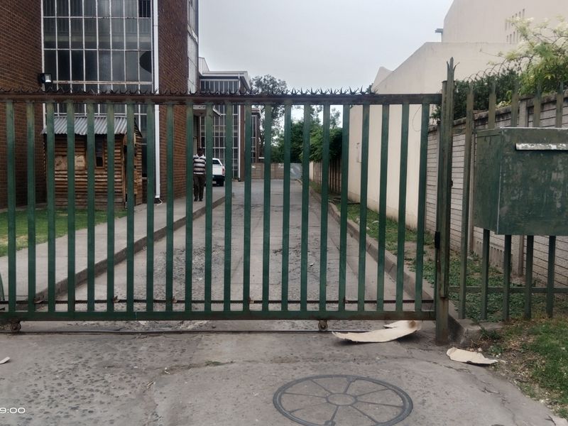 Front entrance view of the property featuring a metal security gate, perimeter wall with spiked fencing, and a concrete driveway.