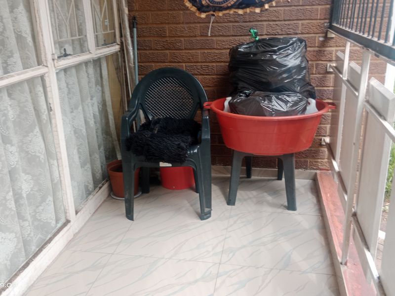 A small balcony area featuring tiled flooring, a brick feature wall, and a metal balustrade, accessible via a sliding glass door.