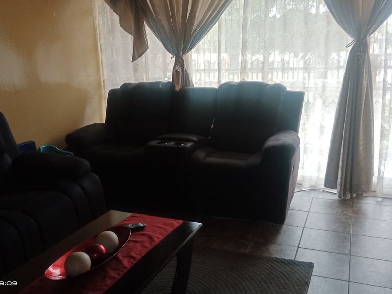 A living room area featuring tiled flooring and a large window with curtains, providing natural light to the space.