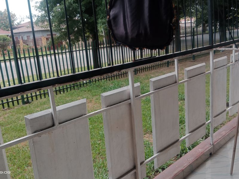 A view from a tiled balcony overlooking a residential street, featuring a metal balustrade and brick wall finish.