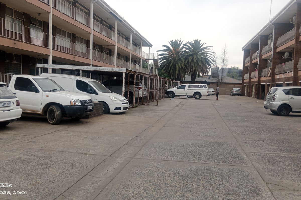 Exterior view of a multi-story residential flat complex featuring paved parking areas and covered parking bays.